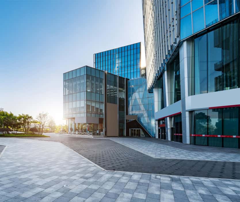 Modern glass office buildings with reflective windows and a spacious paved plaza in front, expertly maintained by key property management, photographed on a sunny day.